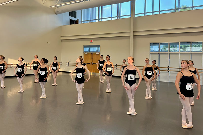 Dancers standing in fifth position in the center of the studio for an audition.