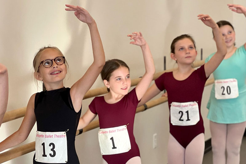 Young dancers at the barre with audition numbers on their leotards. 