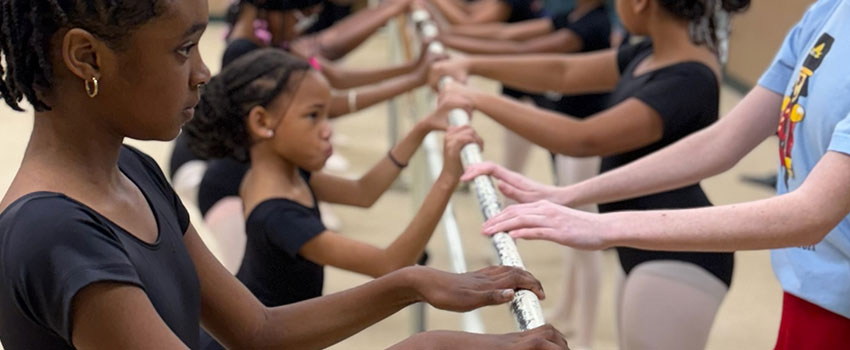 Young dancers with hands on the ballet barre.