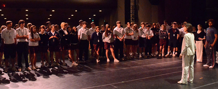 Director speaking to school students on an empty stage for a tour of theater.